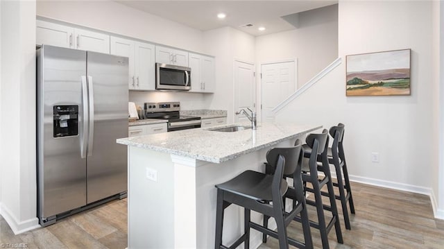 kitchen featuring a center island with sink, a kitchen breakfast bar, stainless steel appliances, light hardwood / wood-style floors, and white cabinets