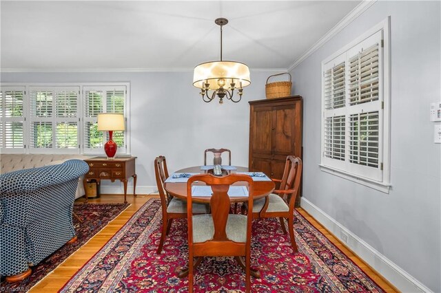 dining area featuring crown molding, wood-type flooring, and an inviting chandelier