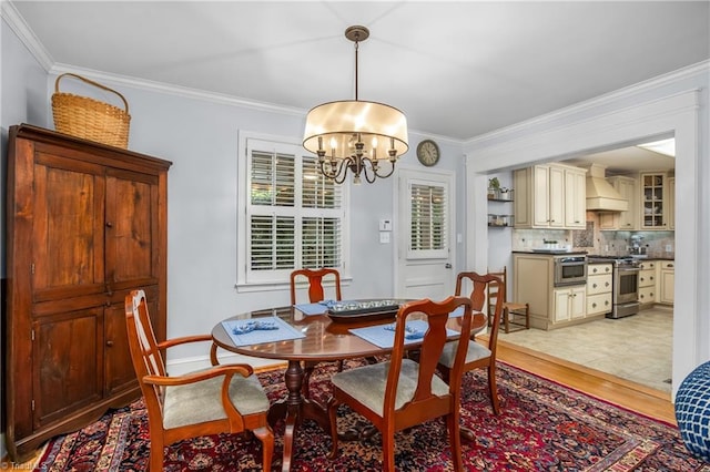 dining area with light hardwood / wood-style flooring, ornamental molding, and an inviting chandelier