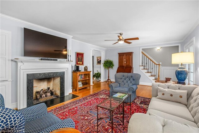 living room with a high end fireplace, light hardwood / wood-style flooring, ceiling fan, and crown molding