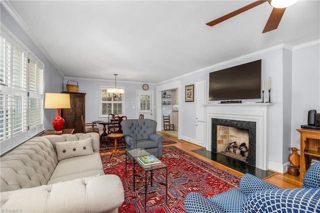 living room featuring ceiling fan with notable chandelier, a premium fireplace, light wood-type flooring, and a healthy amount of sunlight