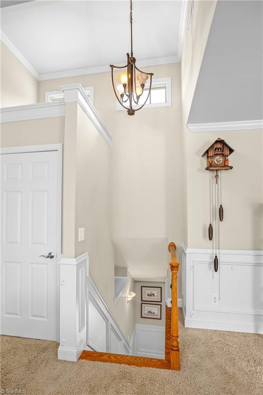 staircase with carpet, crown molding, and a chandelier