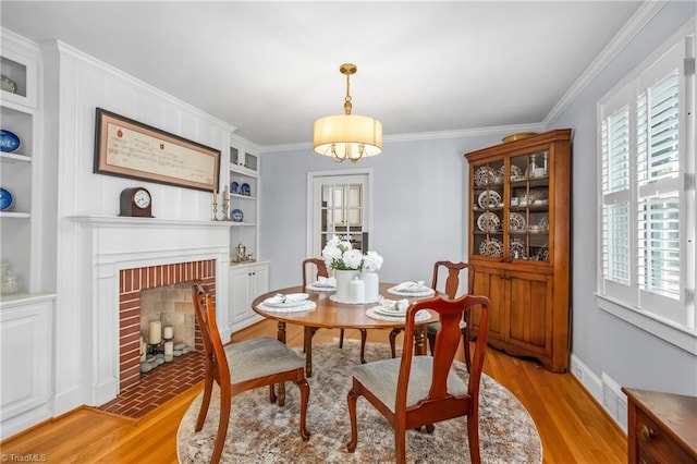 dining area with a fireplace, light wood-type flooring, crown molding, and a wealth of natural light