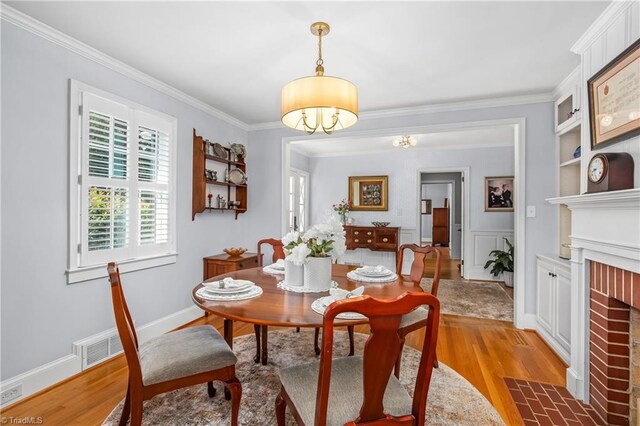 dining room with crown molding, light hardwood / wood-style flooring, a brick fireplace, and built in features