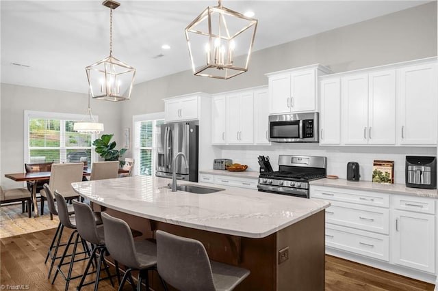 kitchen with stainless steel appliances, a kitchen island with sink, a sink, and a chandelier