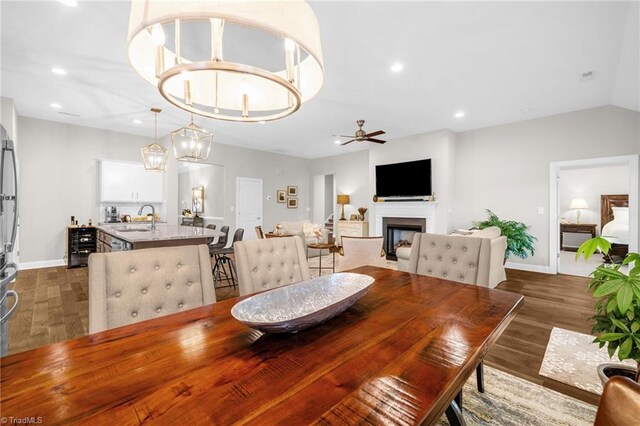 dining space featuring ceiling fan with notable chandelier, a fireplace, baseboards, dark wood-style flooring, and recessed lighting