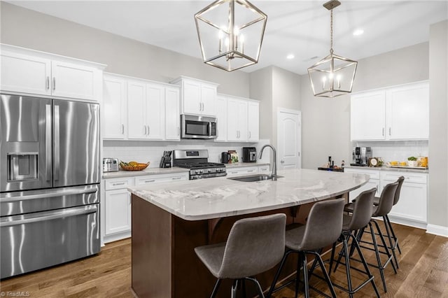 kitchen featuring an island with sink, a sink, decorative backsplash, a chandelier, and appliances with stainless steel finishes