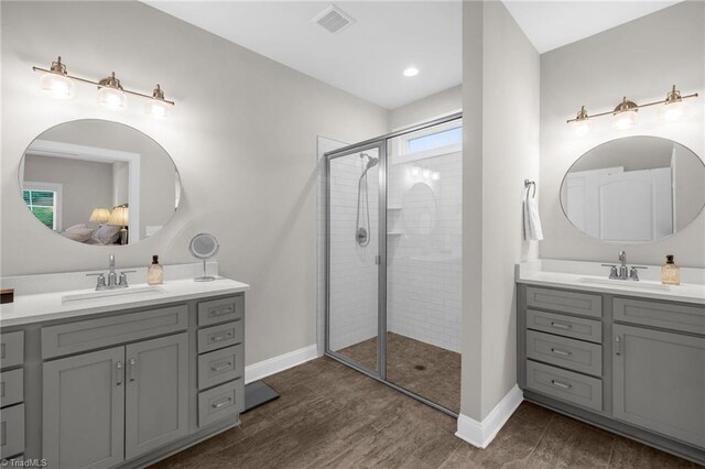 full bath featuring baseboards, two vanities, a sink, and tiled shower