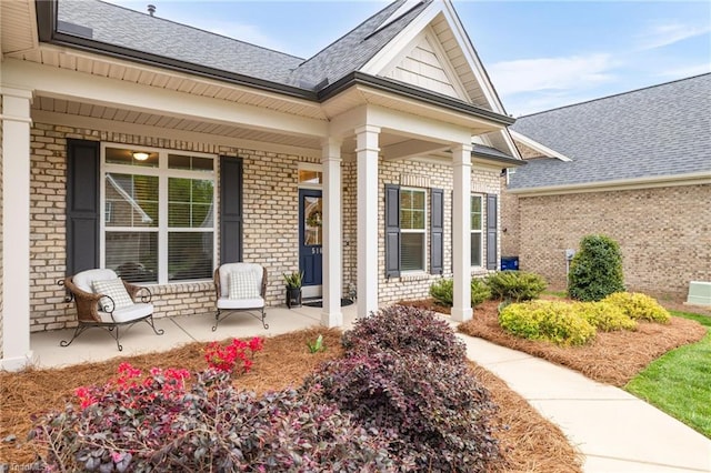 property entrance with brick siding, a porch, and a shingled roof