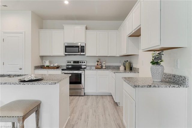 kitchen featuring white cabinets, appliances with stainless steel finishes, light wood-style floors, and light stone countertops