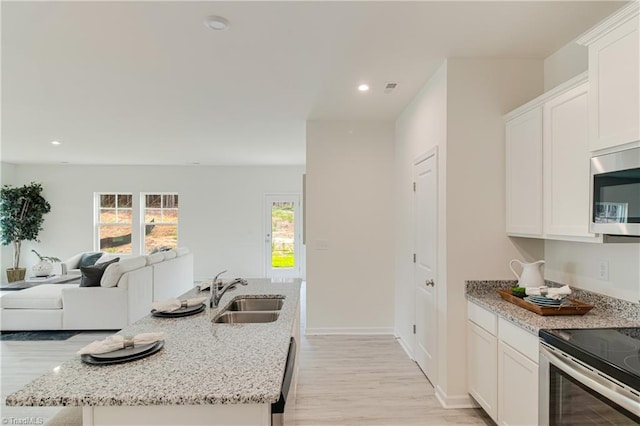 kitchen featuring open floor plan, recessed lighting, white cabinets, stainless steel appliances, and a sink