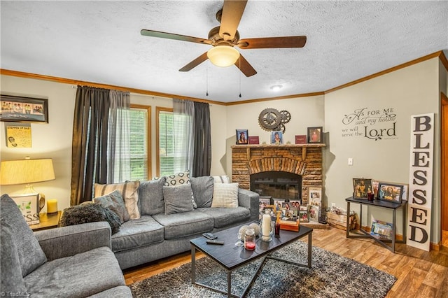 living room featuring a brick fireplace, a textured ceiling, ceiling fan, crown molding, and hardwood / wood-style floors