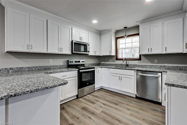 kitchen featuring light wood finished floors, hanging light fixtures, stainless steel appliances, white cabinetry, and a sink