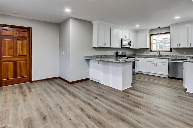 kitchen featuring light stone counters, decorative light fixtures, stainless steel appliances, light wood-style floors, and white cabinetry