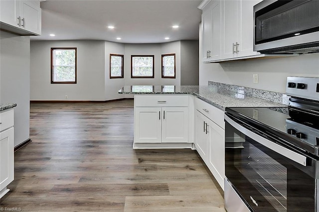 kitchen featuring white cabinets, a peninsula, light stone countertops, stainless steel appliances, and light wood-style floors