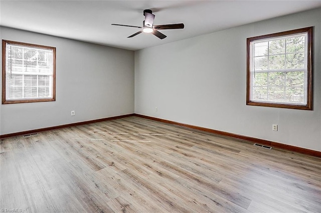 spare room with visible vents, light wood-type flooring, a ceiling fan, and baseboards