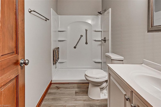 bathroom featuring toilet, wood finished floors, vanity, baseboards, and a shower