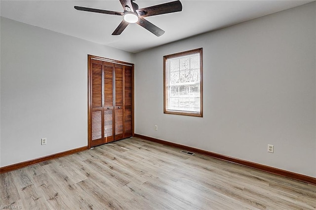 unfurnished bedroom featuring ceiling fan, visible vents, baseboards, a closet, and light wood finished floors