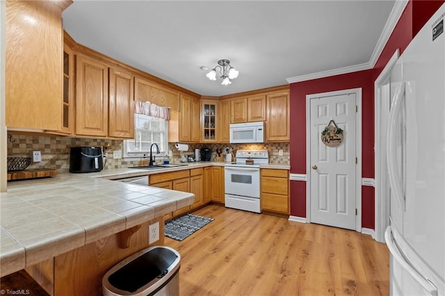 kitchen with glass insert cabinets, crown molding, a chandelier, white appliances, and a sink