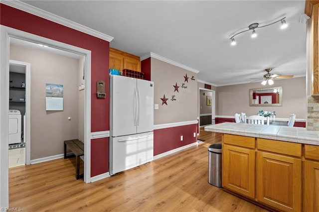 kitchen with a ceiling fan, freestanding refrigerator, light wood-style floors, brown cabinetry, and crown molding