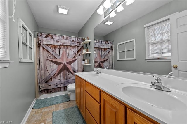 bathroom featuring a sink, toilet, stone tile flooring, and double vanity