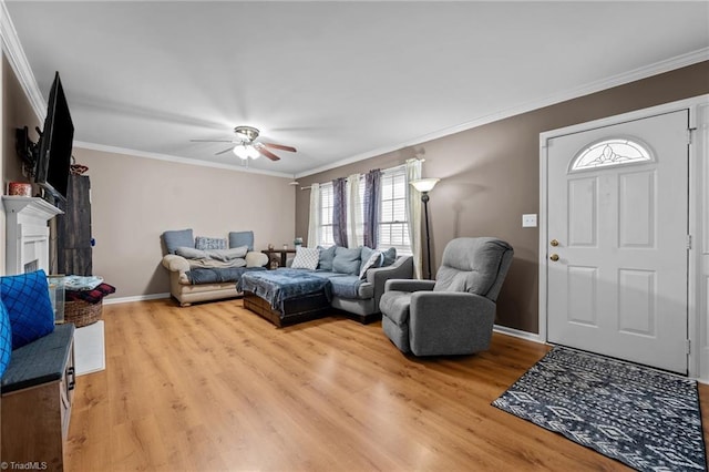 living room featuring baseboards, a fireplace, ornamental molding, ceiling fan, and light wood-style floors