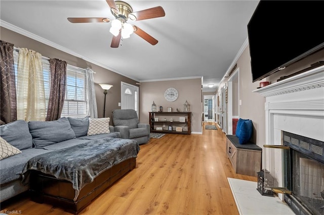 living area with a ceiling fan, baseboards, light wood finished floors, a fireplace, and crown molding