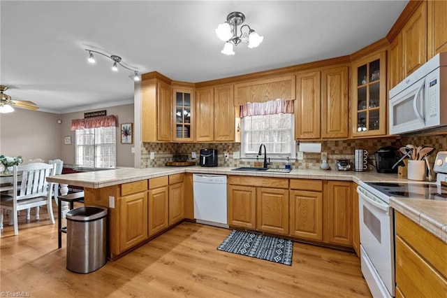 kitchen featuring white appliances, a peninsula, a sink, tile counters, and light wood-style floors