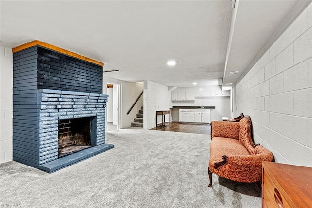 living room featuring a brick fireplace, stairs, dark carpet, concrete block wall, and recessed lighting