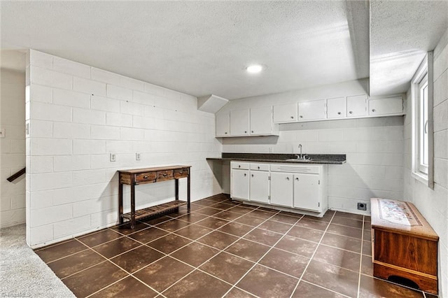 kitchen featuring a sink, white cabinets, concrete block wall, a textured ceiling, and dark countertops