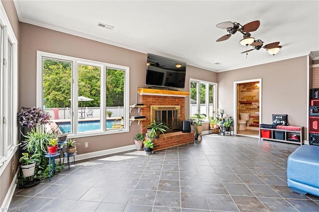 living area with a ceiling fan, a fireplace, crown molding, tile patterned floors, and baseboards
