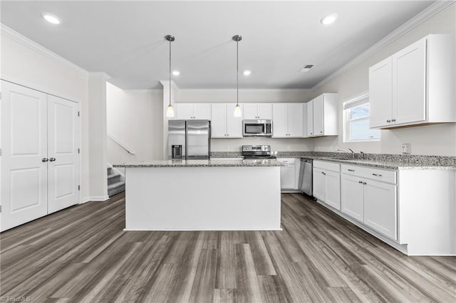 kitchen with appliances with stainless steel finishes, a center island, light stone countertops, white cabinetry, and pendant lighting