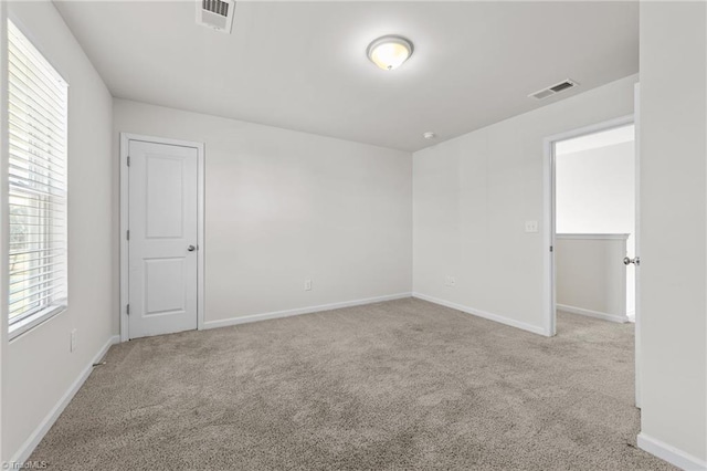 empty room featuring baseboards, visible vents, and light colored carpet