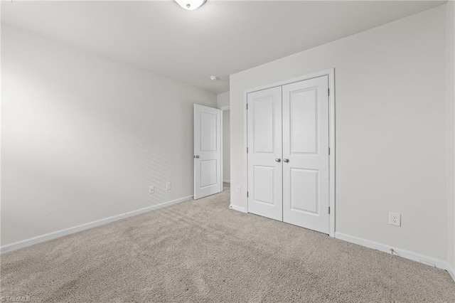 unfurnished bedroom with a closet, light carpet, and baseboards