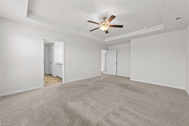 unfurnished bedroom with light carpet, a raised ceiling, visible vents, and baseboards