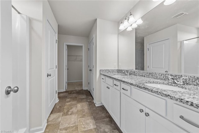 full bath featuring a sink, visible vents, baseboards, a spacious closet, and double vanity