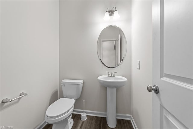 half bath with baseboards, a sink, toilet, and wood finished floors