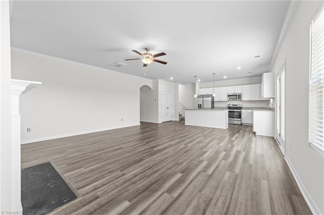 unfurnished living room with arched walkways, ceiling fan, wood finished floors, baseboards, and crown molding