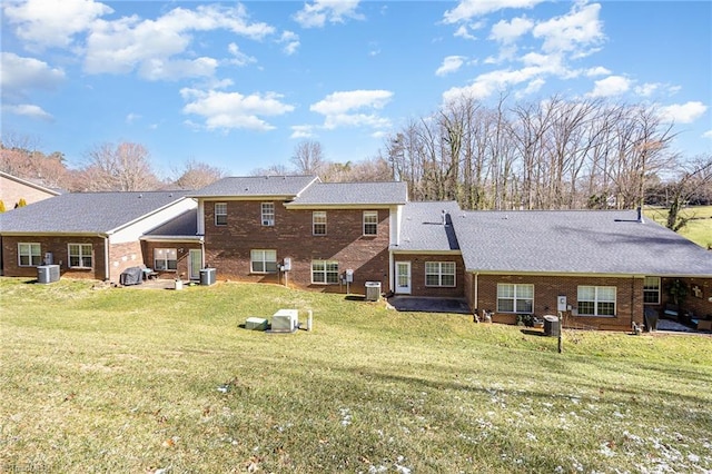 rear view of property featuring cooling unit, brick siding, and a lawn