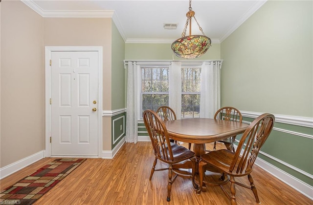 dining area featuring baseboards, light wood finished floors, visible vents, and crown molding