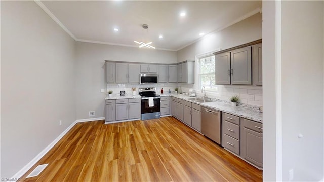 kitchen with gray cabinets, stainless steel appliances, crown molding, and a sink