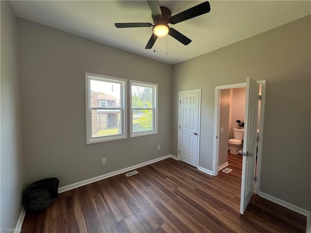 unfurnished bedroom featuring dark wood-style flooring, visible vents, ensuite bath, and baseboards