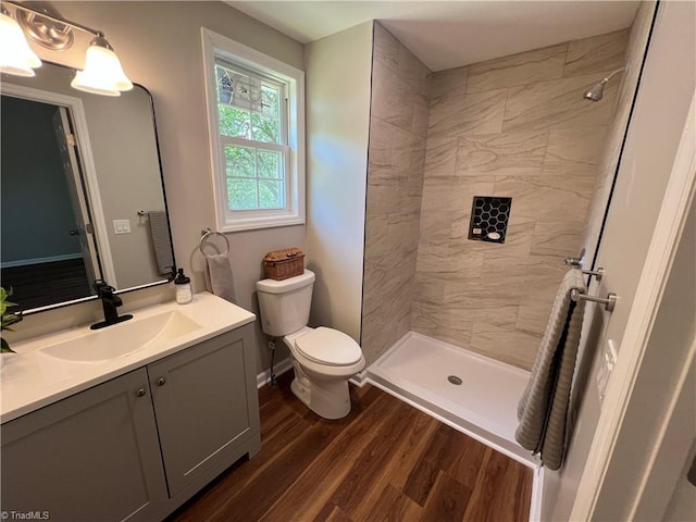bathroom featuring toilet, wood finished floors, vanity, and tiled shower