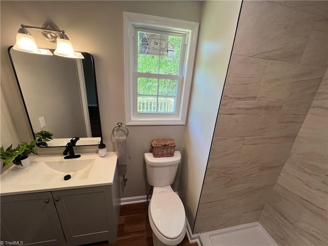 bathroom featuring baseboards, a tile shower, toilet, and vanity