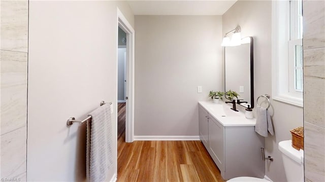 half bath featuring wood finished floors, toilet, vanity, and baseboards