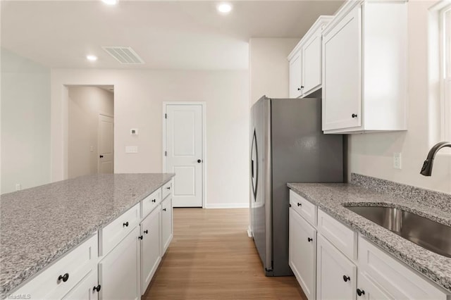 kitchen featuring stainless steel refrigerator with ice dispenser, sink, light stone counters, light hardwood / wood-style floors, and white cabinets