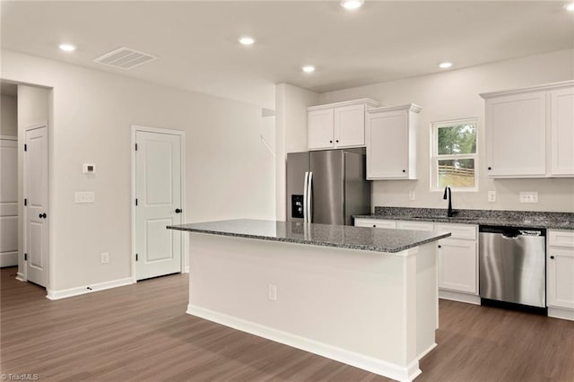 kitchen with stainless steel appliances, dark stone counters, a kitchen island, and white cabinets