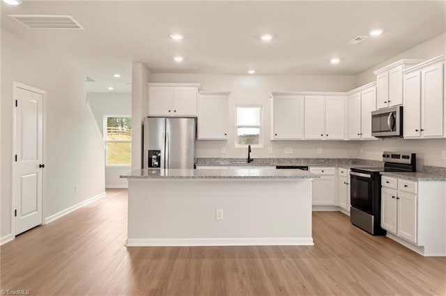 kitchen with white cabinetry, stainless steel appliances, a center island, and light stone countertops