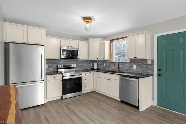 kitchen with white cabinetry, stainless steel appliances, tasteful backsplash, sink, and light wood-type flooring