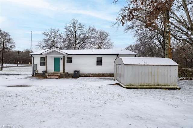 snow covered property featuring central AC and a storage shed